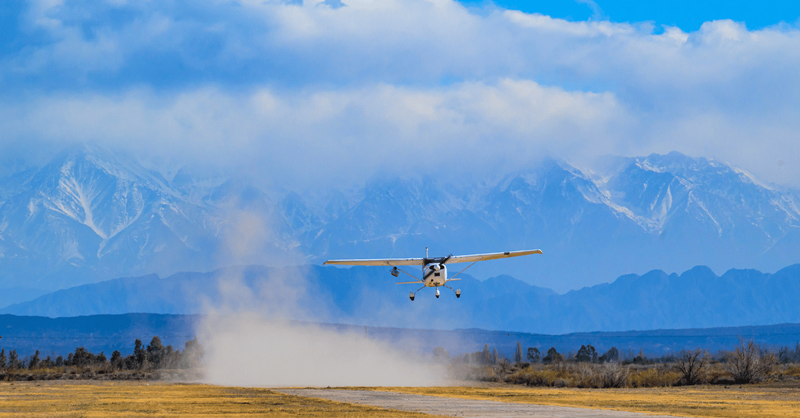Plane carrying Bridger GML device flying over a field in front of snowy mountains