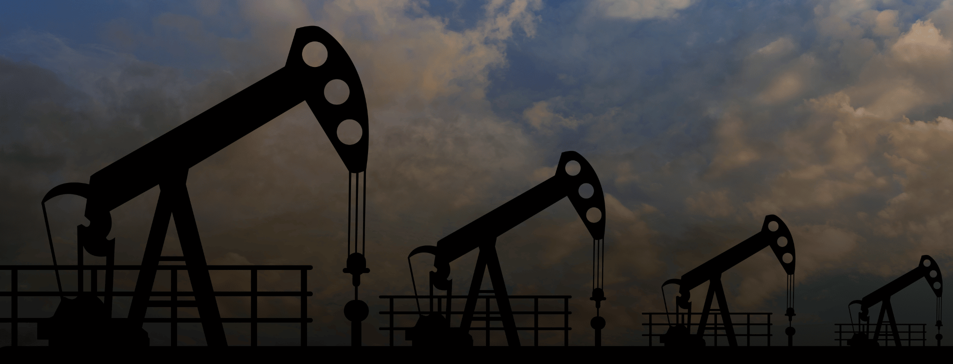 Four oil drills lined up against partly cloudy sky